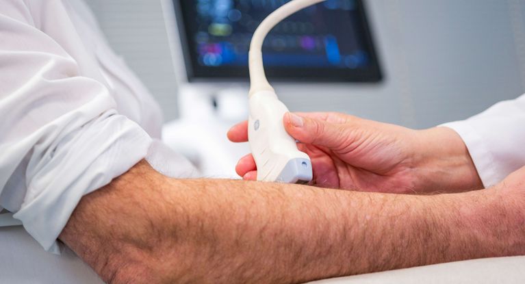 Ärztin untersucht Arm eines Patienten mit Ultraschall