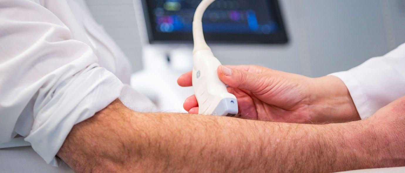 Ärztin untersucht Arm eines Patienten mit Ultraschall