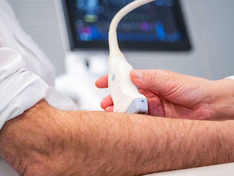 Ärztin untersucht Arm eines Patienten mit Ultraschall